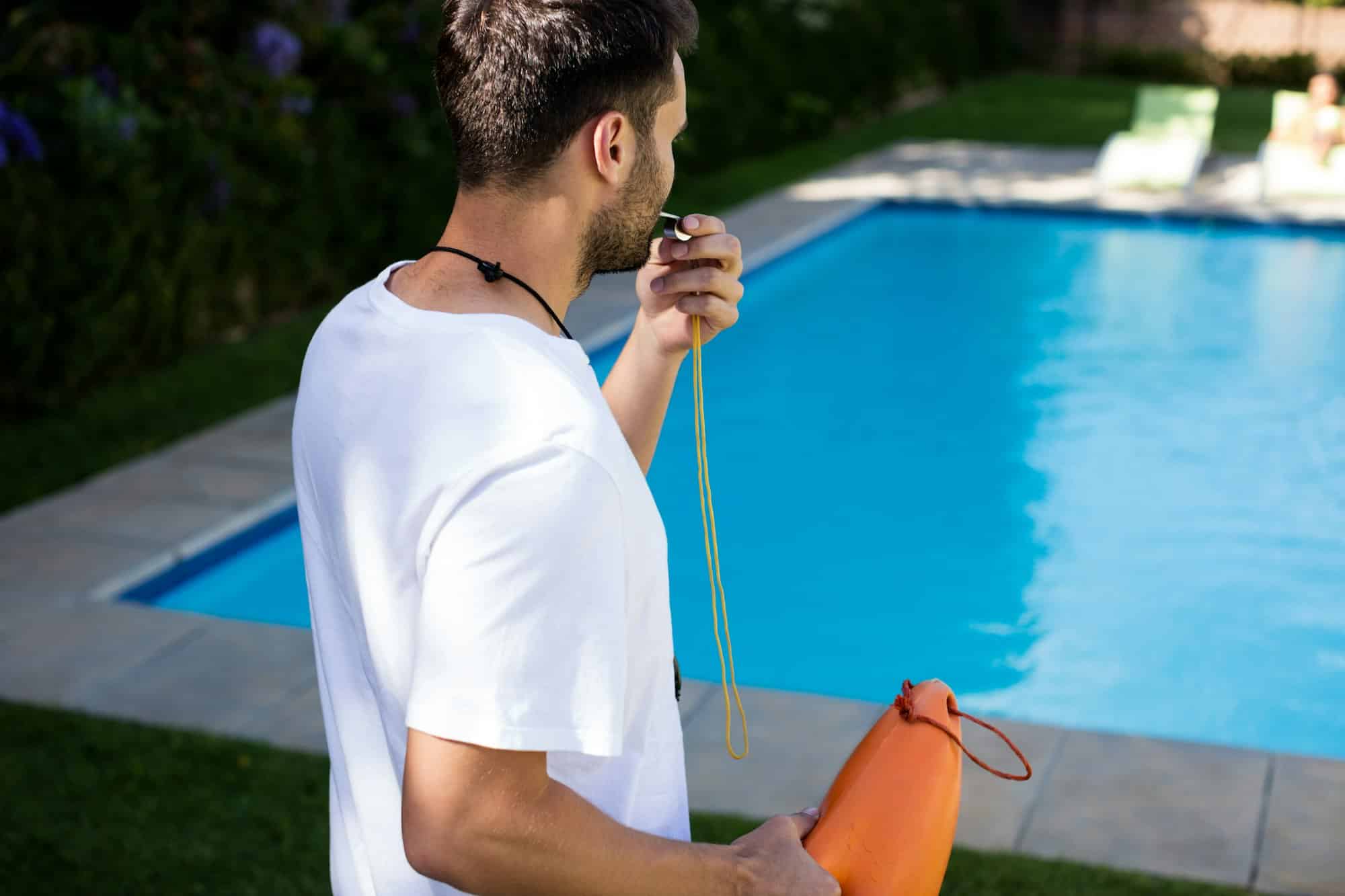 Lifeguard blowing whistle at poolside